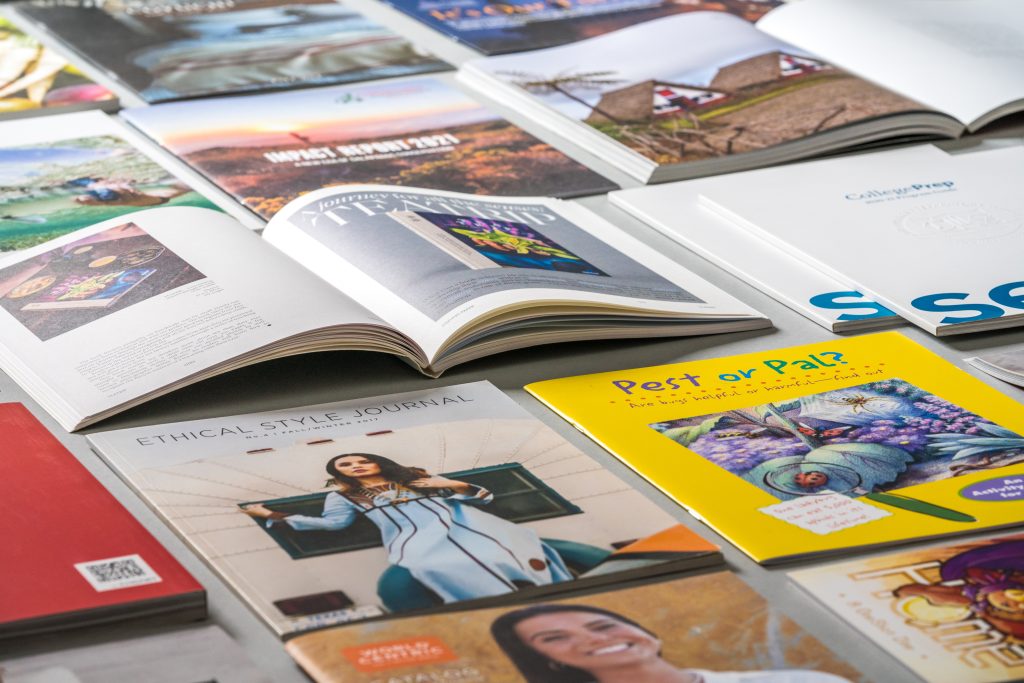 A variety of magazines and zines on a table. Some are open and some are closed.