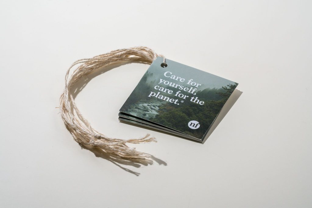 Square recycled hang tag printed with a misty forest photo, strung with natural twine