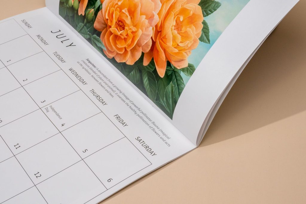Custom calendar opened to a July spread with floral artwork and a monthly date grid