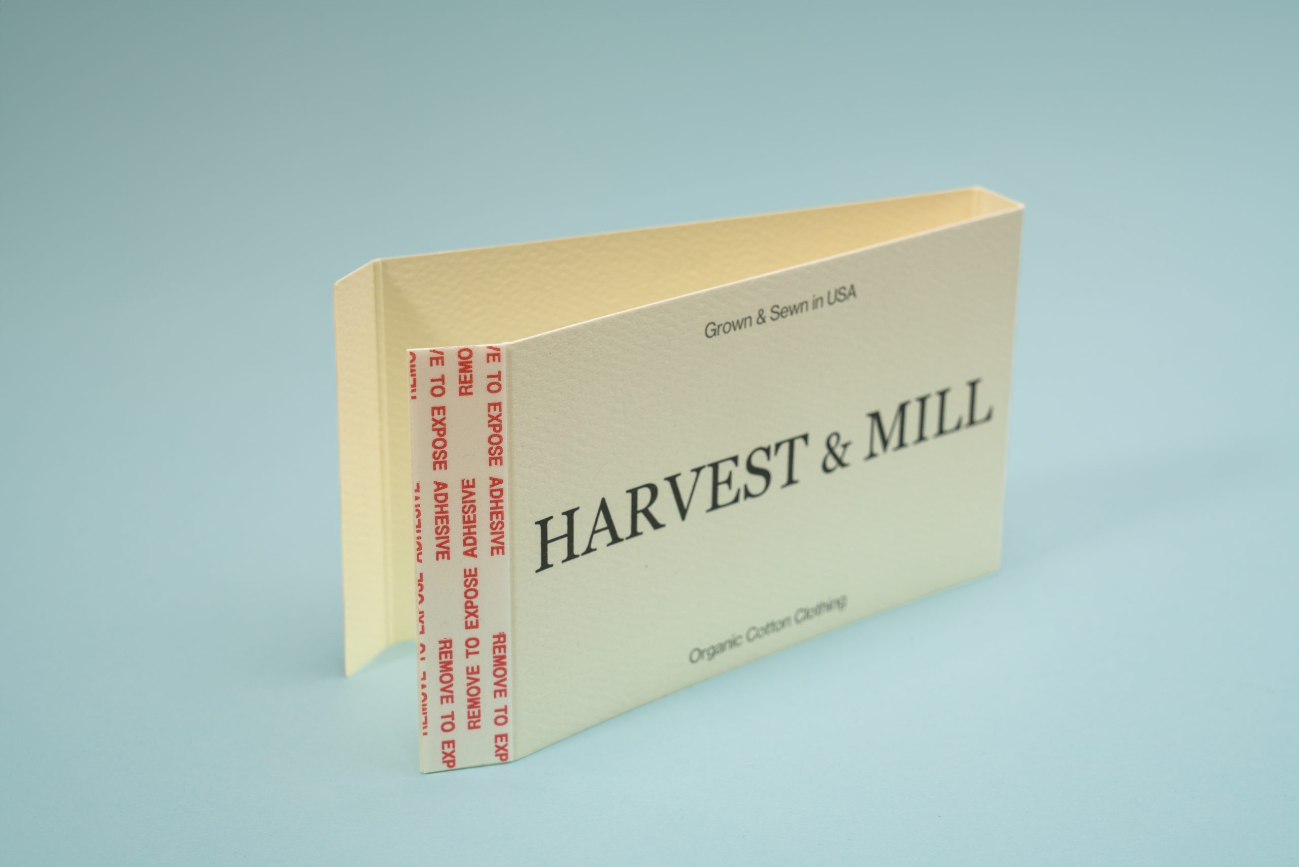 A cream-colored, self-adhesive paper envelope or sleeve standing slightly open against a plain light blue background.