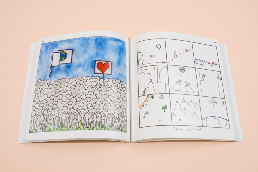 An open illustrated book showing a large crowd of stick-figure people holding flags under a blue sky on the left page, and a comic grid panel sequence labeled "Follow your heart" on the right page.