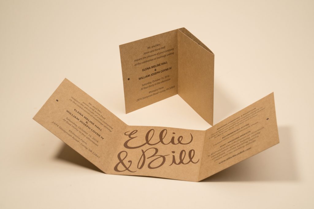 A kraft paper accordion-fold invitation standing upright on a beige background, with script lettering reading "Ellie & Bill" on the front panel and wedding event details printed across the inner panels.